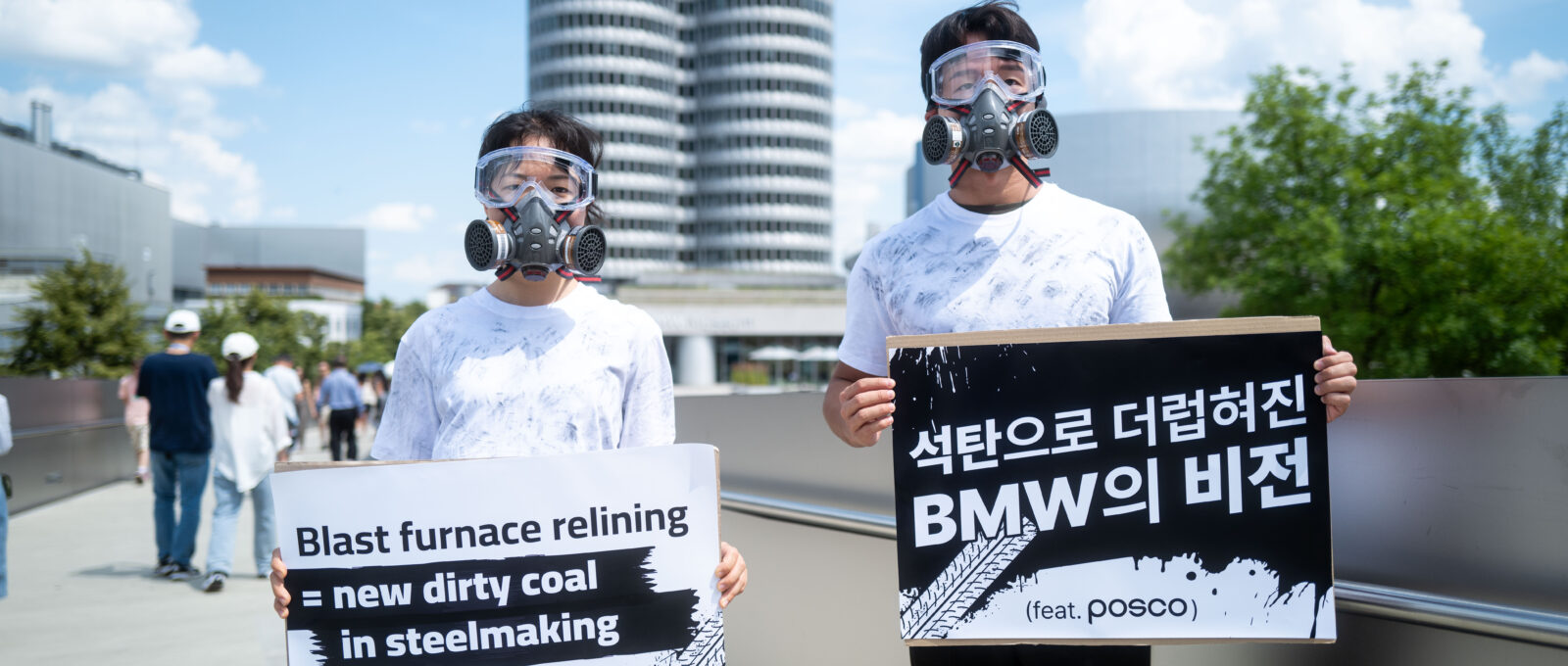 Activists stand in front of POSCO facility with signs urging POSCO to drop its plans to reline coal blast furnaces
